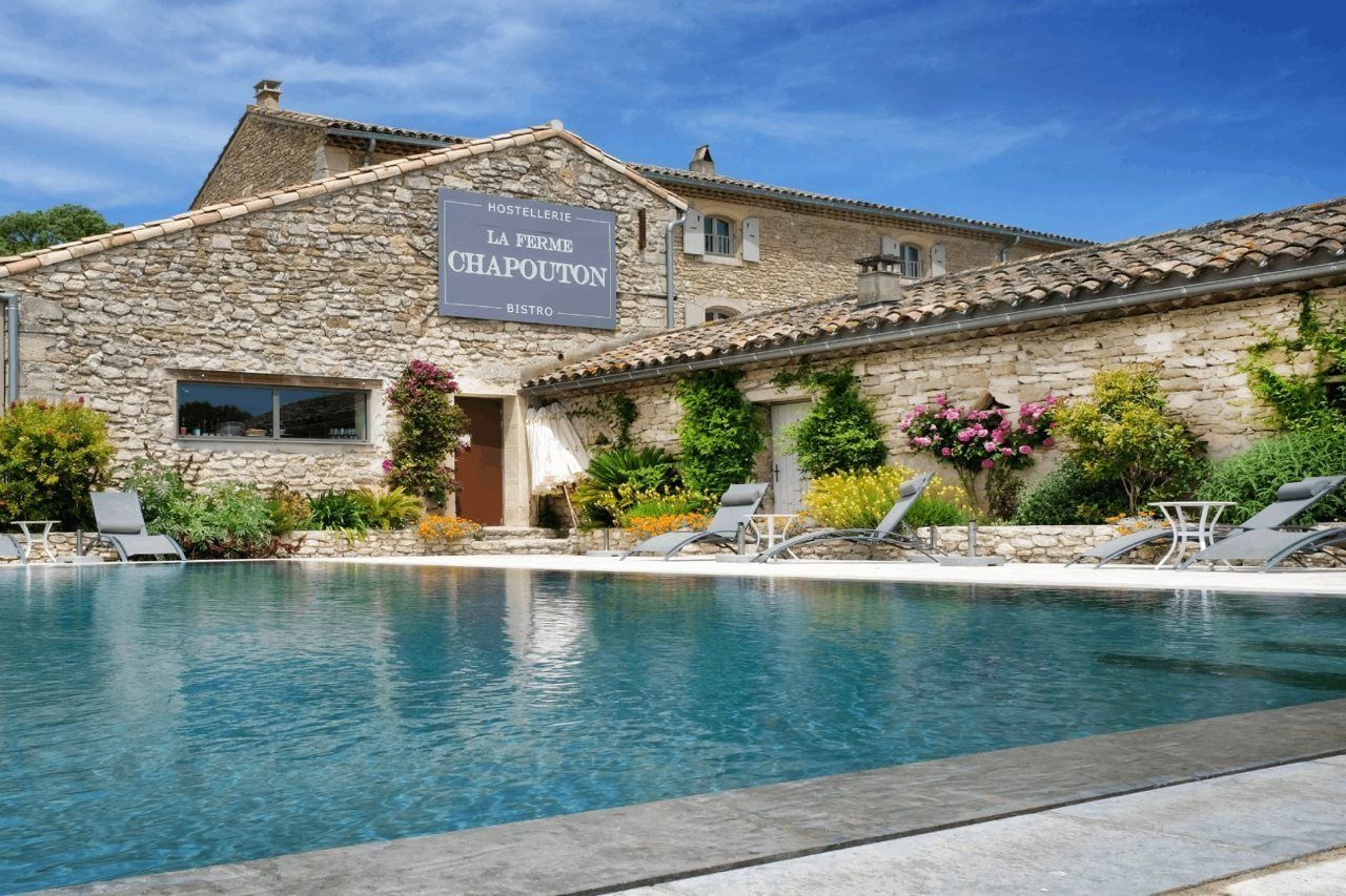 A stone building with a sign for 'La Ferme Chapouton' and a pool area with lounge chairs.