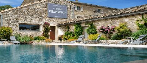 A stone building with a sign for 'La Ferme Chapouton' and a pool area with lounge chairs.