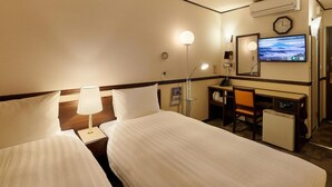 Quarto de hotel com duas camas, uma escrivaninha, uma cadeira, uma televisão, um relógio e um aparelho de ar condicionado.