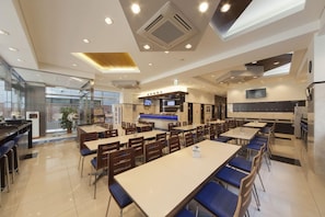 A modern restaurant with multiple dining tables and chairs, a kitchen area, and a large window providing natural light.