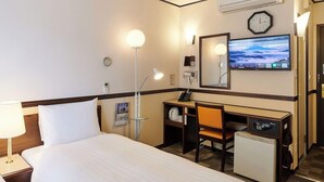 Quarto de hotel com cama, escrivaninha, cadeira e um pequeno frigorífico.