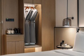 A hotel room with a wooden wardrobe, a bed, a bedside table with a lamp, and a small round table with a tissue box.