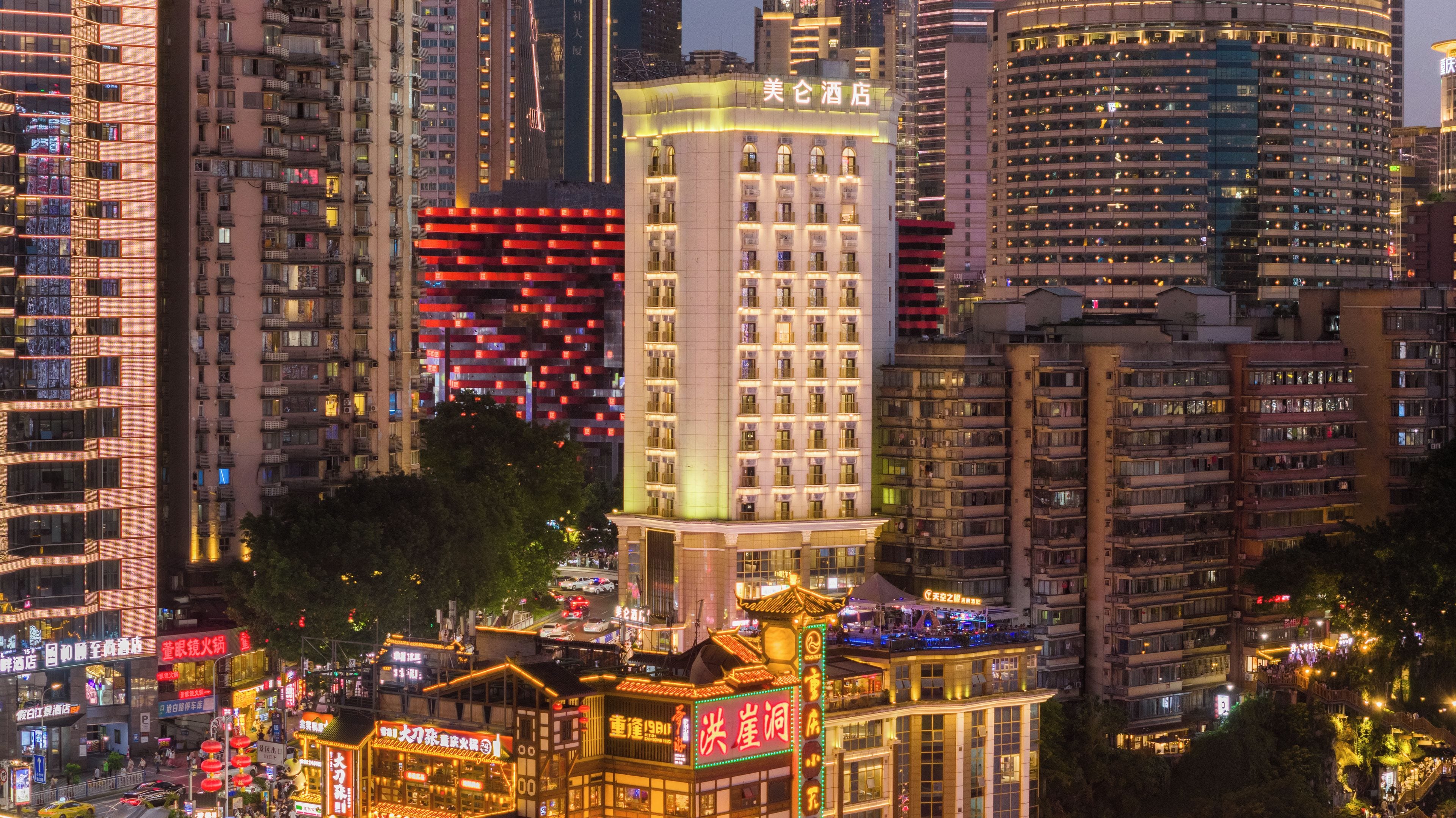 A high-rise hotel with multiple floors, a traditional-style building with a pagoda roof, and a busy street with illuminated signs.