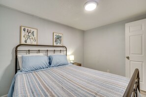Ein Schlafzimmer mit einem Bett, einem Nachttisch, einer Lampe und zwei gerahmten Kunstwerken an der Wand.