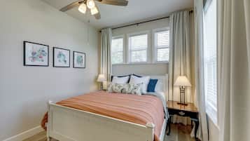 A bedroom with a bed, two bedside tables, a ceiling fan, and three wall-mounted pictures.