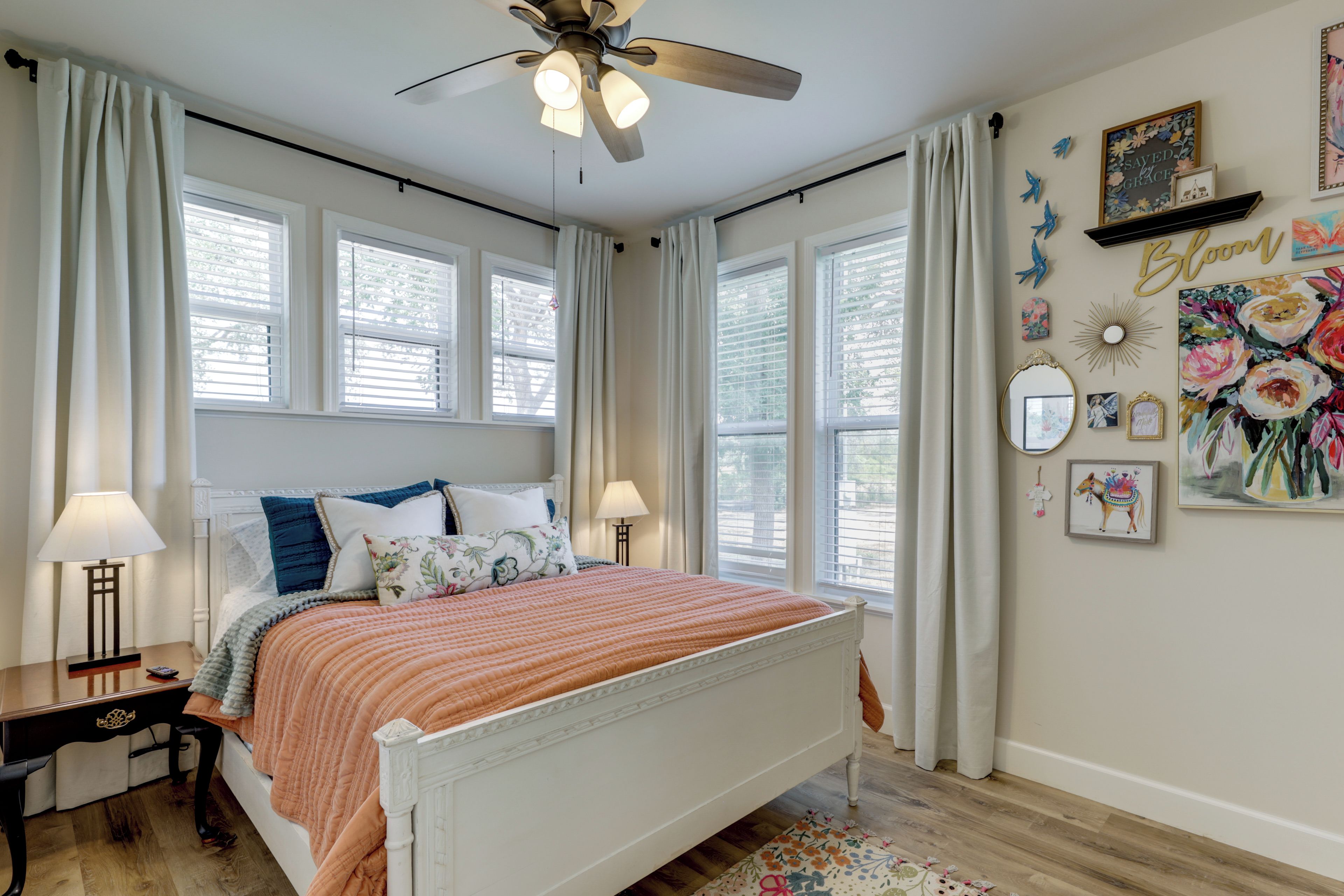 A bedroom with a bed, two bedside tables, a ceiling fan, and a window with curtains.
