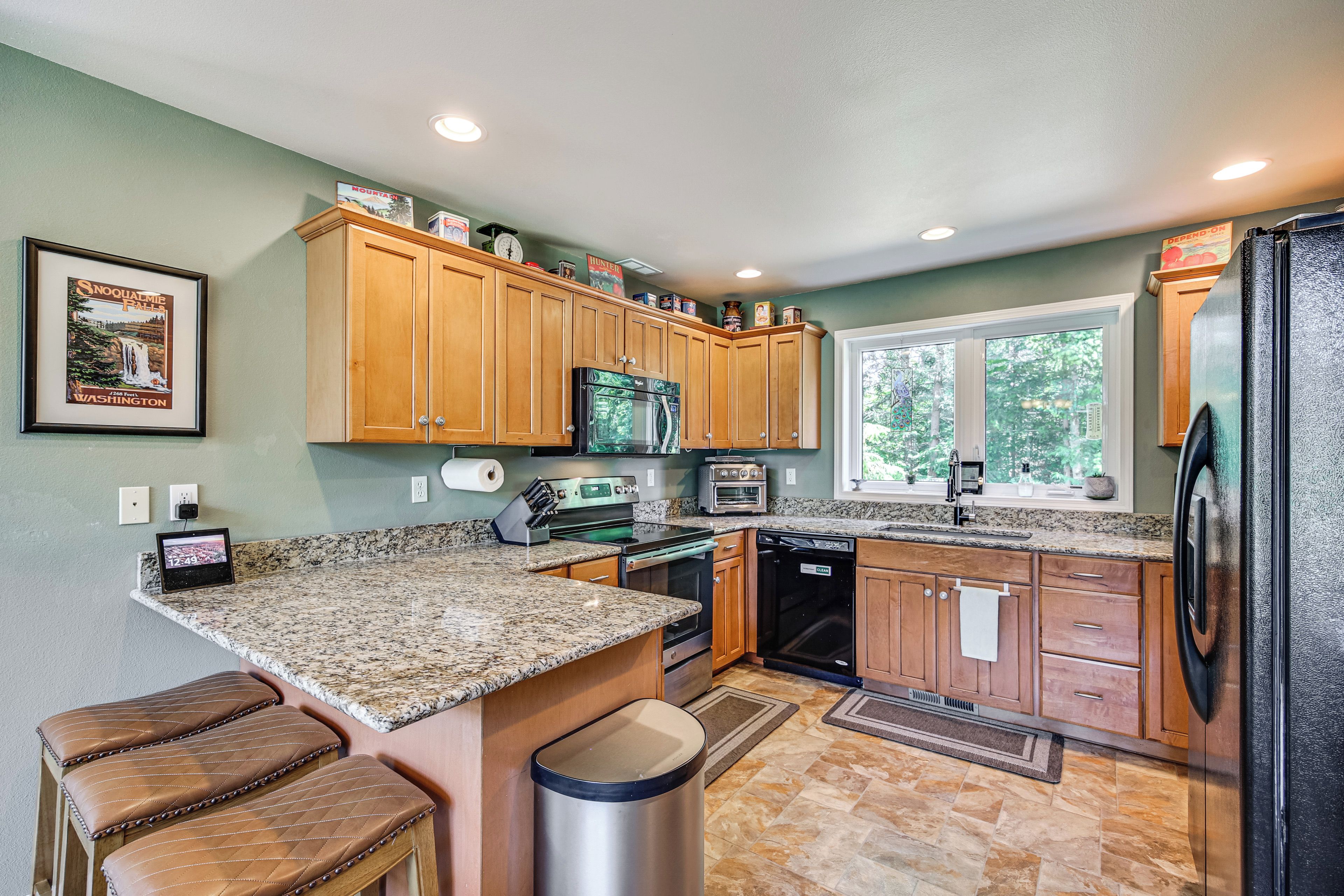 A kitchen with granite countertops, wooden cabinets, stainless steel appliances, and a window providing natural light.