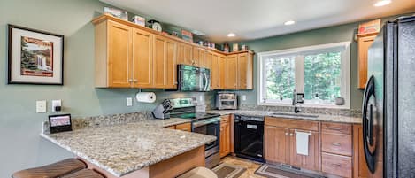 A kitchen with granite countertops, wooden cabinets, stainless steel appliances, and a window providing natural light.