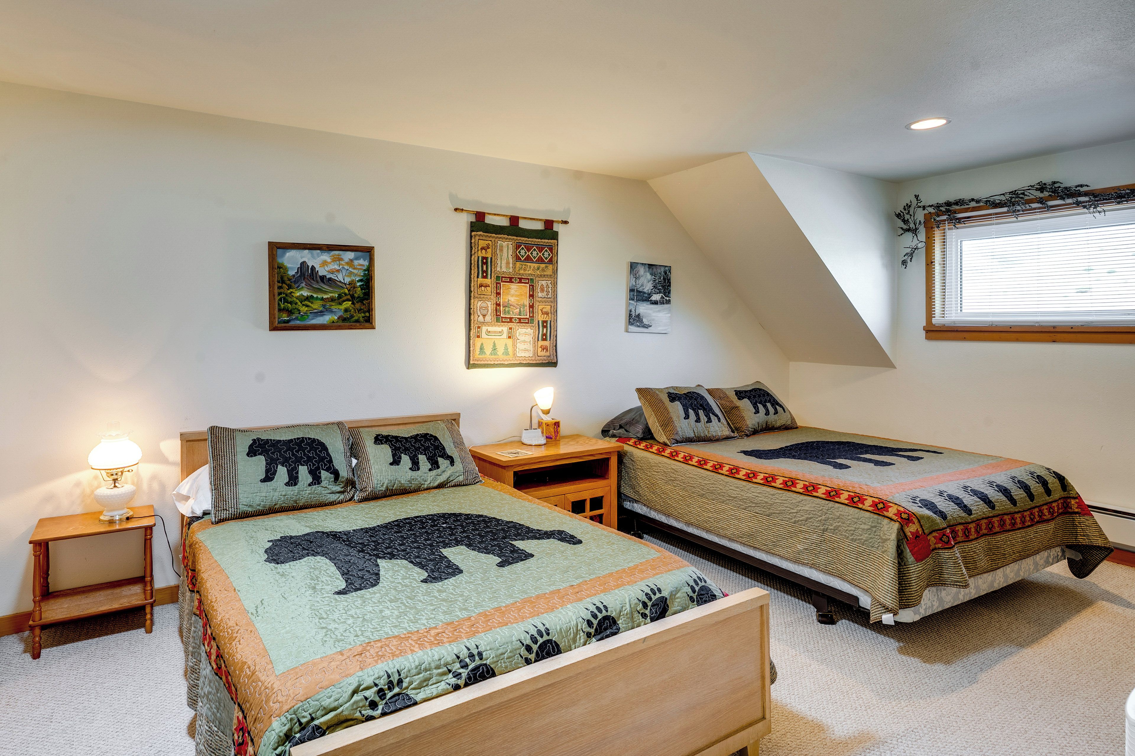 Un dormitorio con dos camas, cada una con colcha temática de osos, una mesita de noche con lámpara y una pared con tres cuadros enmarcados.