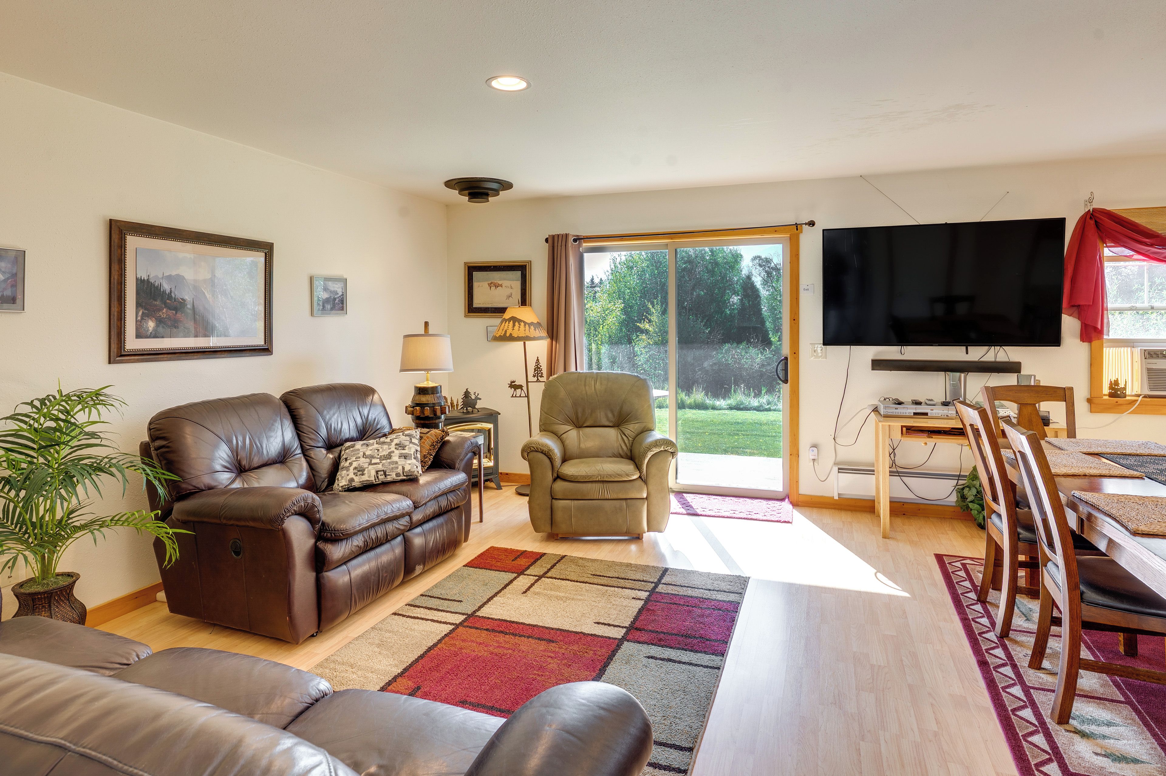 A living room with a brown leather sofa, a green armchair, a TV, and a dining area with a wooden table and chairs.