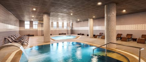 An indoor swimming pool with multiple lanes, lounge chairs, and a ceiling with recessed lighting.