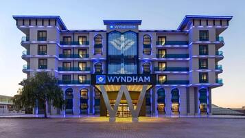 A multi-story hotel with a prominent 'WYNDHAM' sign, featuring a modern architectural design with balconies and a central entrance.