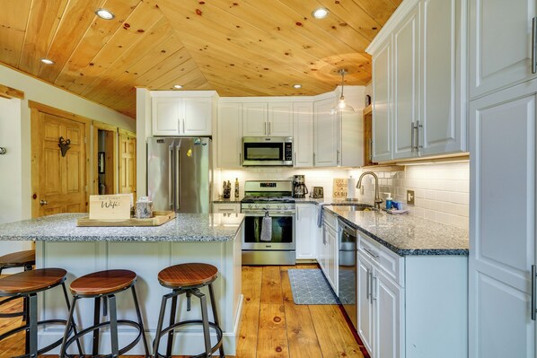 A modern kitchen with white cabinets, stainless steel appliances, and a wooden ceiling.