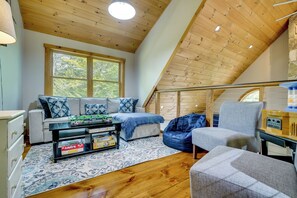 A cozy loft bedroom with a sloped ceiling, a sofa, a chair, a coffee table, and a bookshelf.