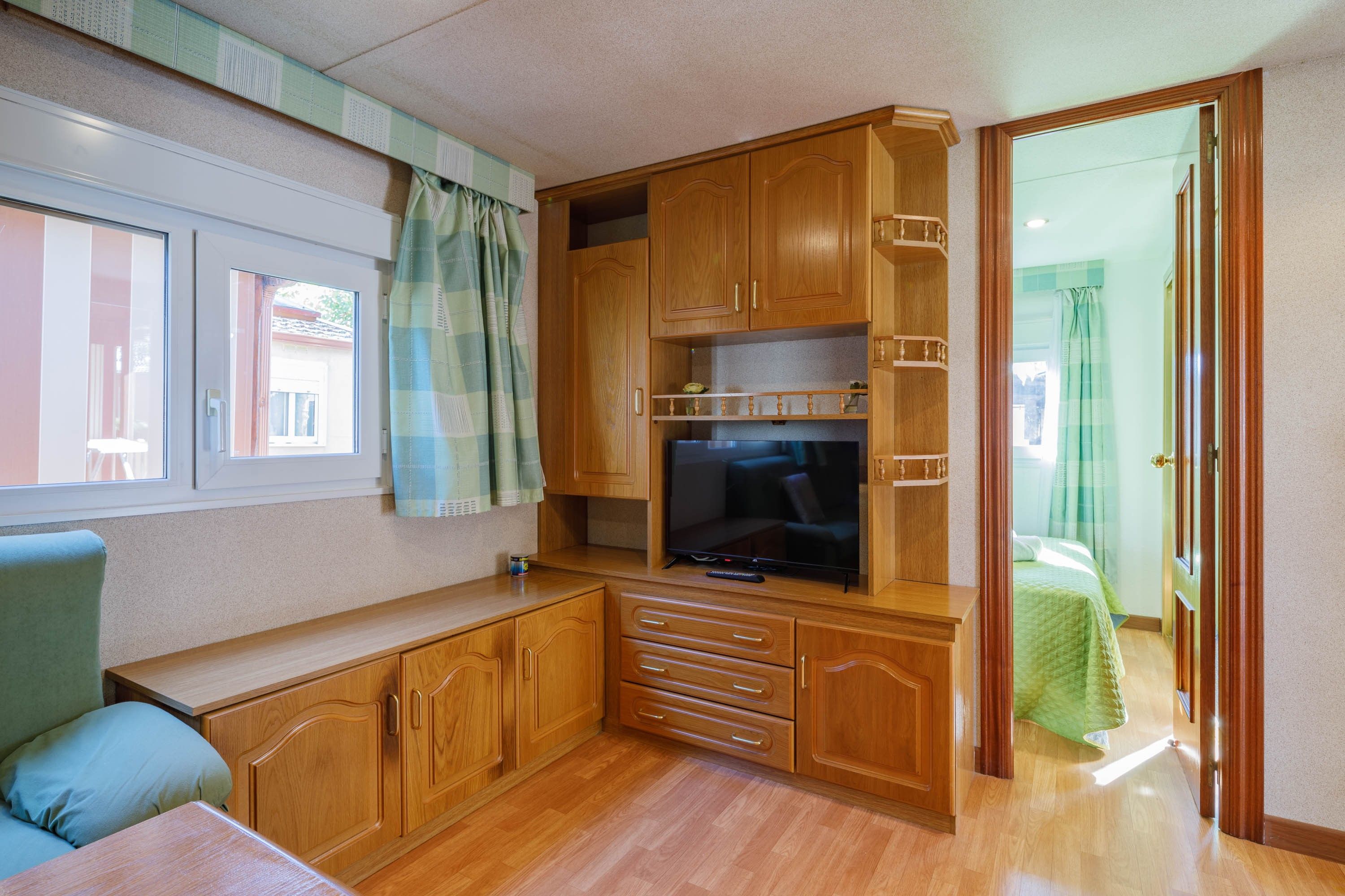 A compact living space with a kitchenette, a television, and a window with curtains.