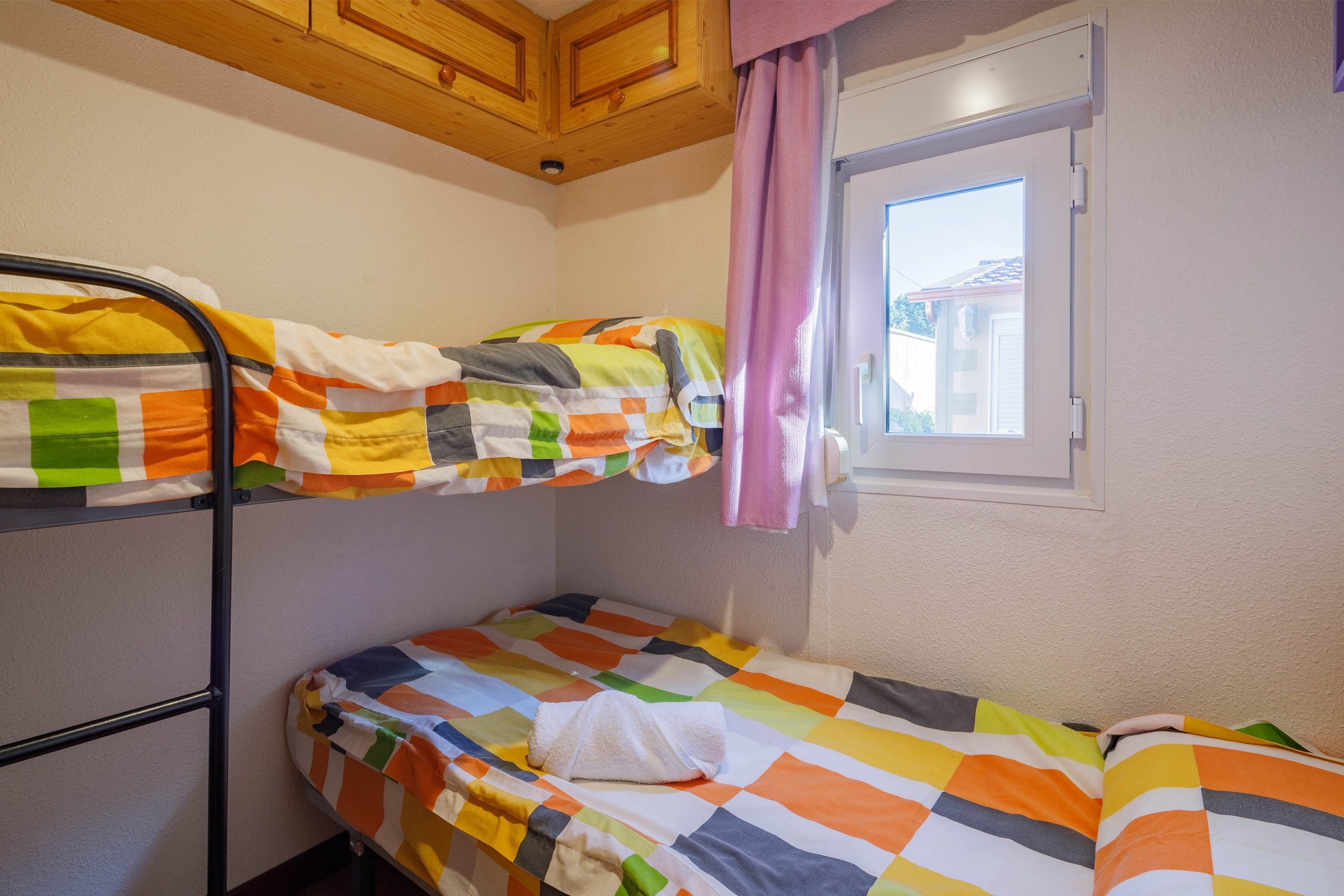 Une chambre de dortoir avec des lits superposés, une fenêtre avec des rideaux et une vue sur l’extérieur.
