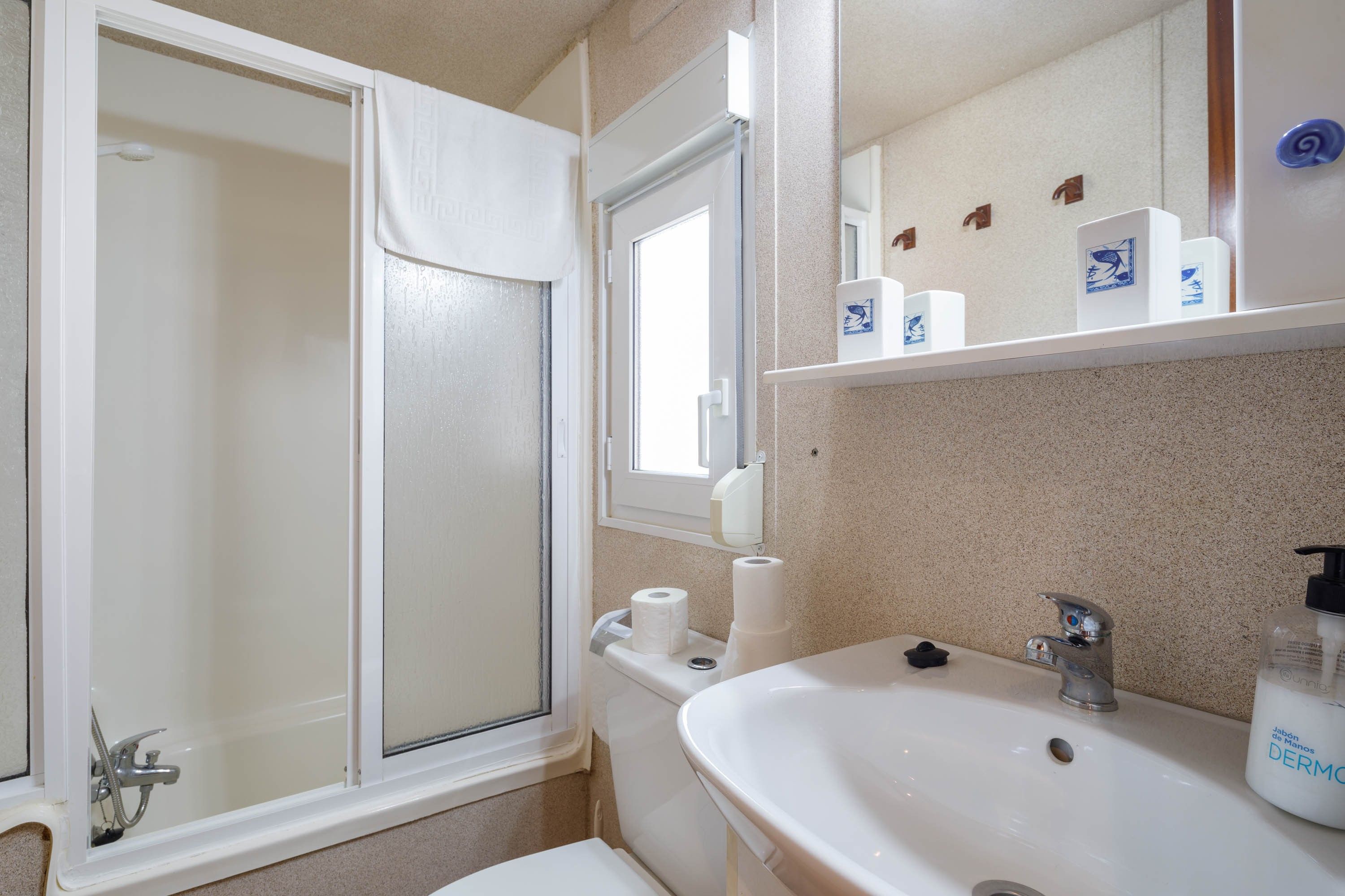 Un baño con ducha, inodoro, lavabo y repisa con artículos de aseo.