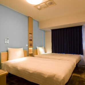 Une chambre d’hôtel avec deux lits, une table de chevet, une étagère fixée au mur et une fenêtre avec des rideaux occultants.