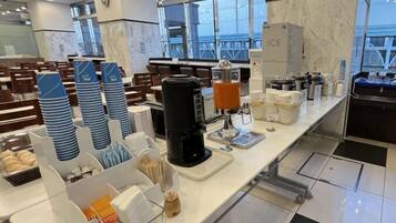 Un área de desayuno de hotel con barra libre, que incluye platos apilados, una estación de café y una variedad de alimentos.