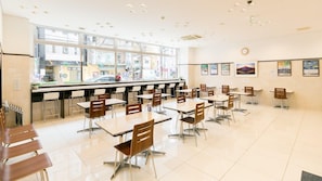A clean, well-lit dining area with multiple tables and chairs, a large window providing a view of the street, and framed pictures on the walls. - Toyoko Inn Sagamihara Ekimae (Sagamihara)