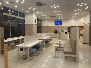A modern cafe with multiple seating options including tables and stools, a digital display, and a self-service kiosk. - Toyoko Inn Sagamihara Ekimae (Sagamihara)