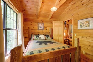 Une chambre dans un chalet en bois, avec un lit recouvert d’une courtepointe à motifs d’ours, une fenêtre avec des rideaux et un tableau encadré accroché au mur.