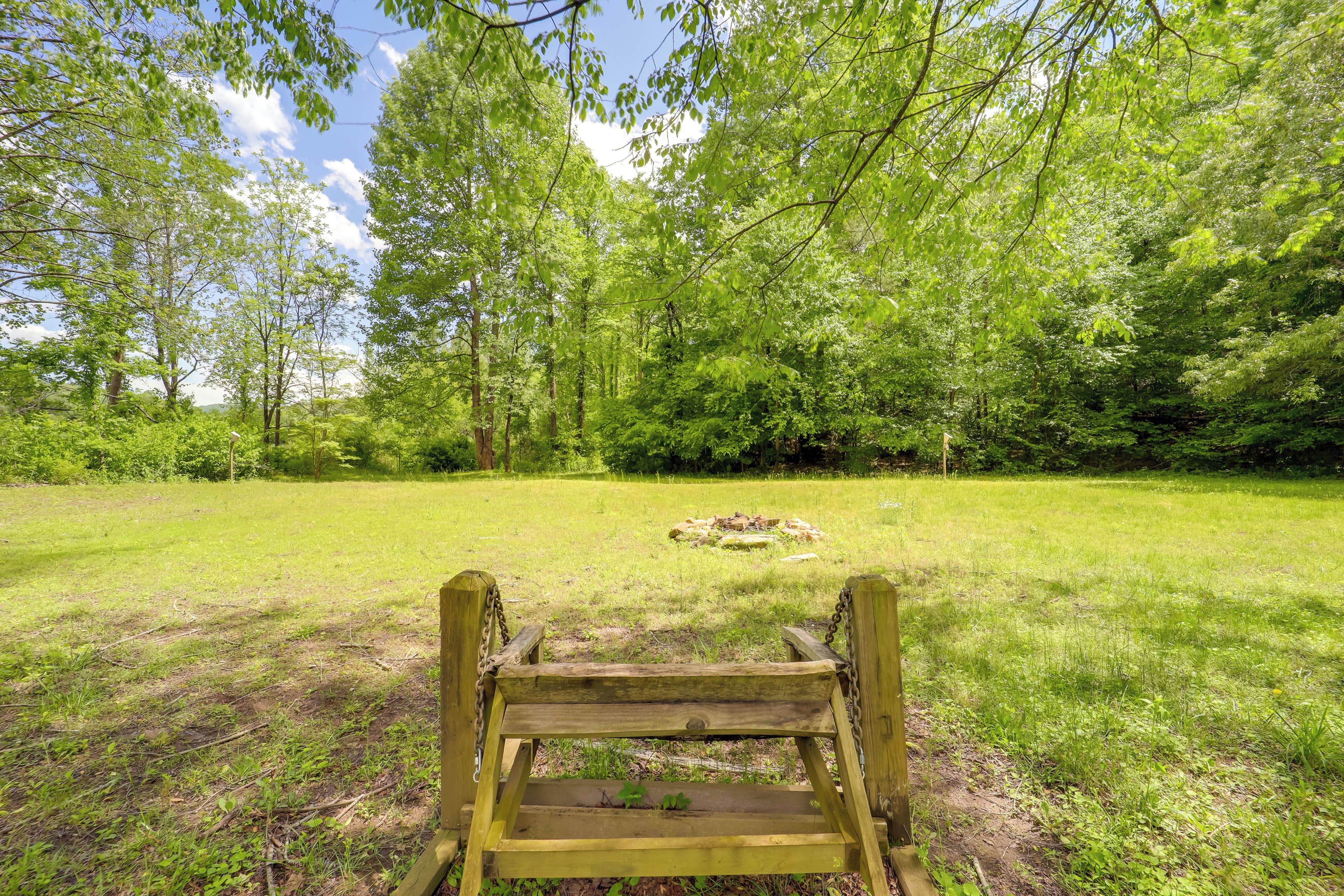 Un banc en bois, situé dans un espace verdoyant, avec des arbres en arrière-plan.
