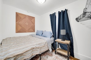 A bedroom with a bed, a wall-mounted wooden panel, a desk with a lamp, and a curtain.