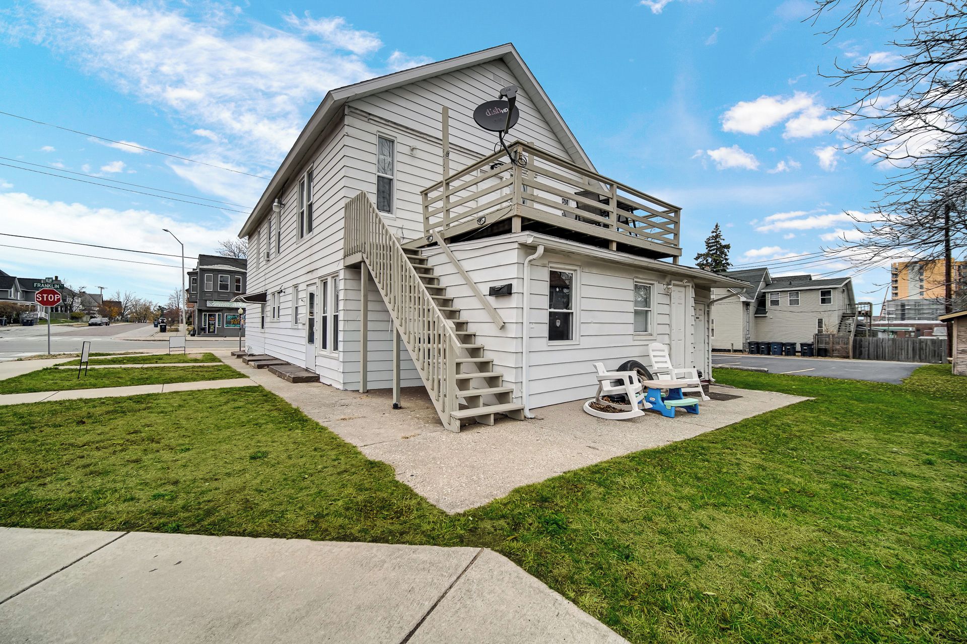 A two-story house with a staircase leading to the upper floor, a satellite dish on the roof, and a small porch area with a chair.
