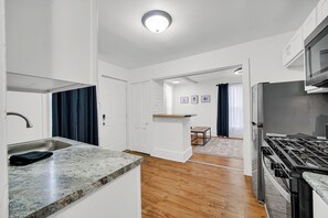 A modern kitchen with a granite countertop, stainless steel appliances, and a wooden floor.