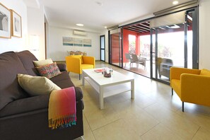 A modern living room with a sofa, coffee table, and yellow chairs. There is a dining area with a table and chairs visible through a glass door. - Beautiful house at Salobre Golf Resort with private pool (San Bartolomé de Tirajana)