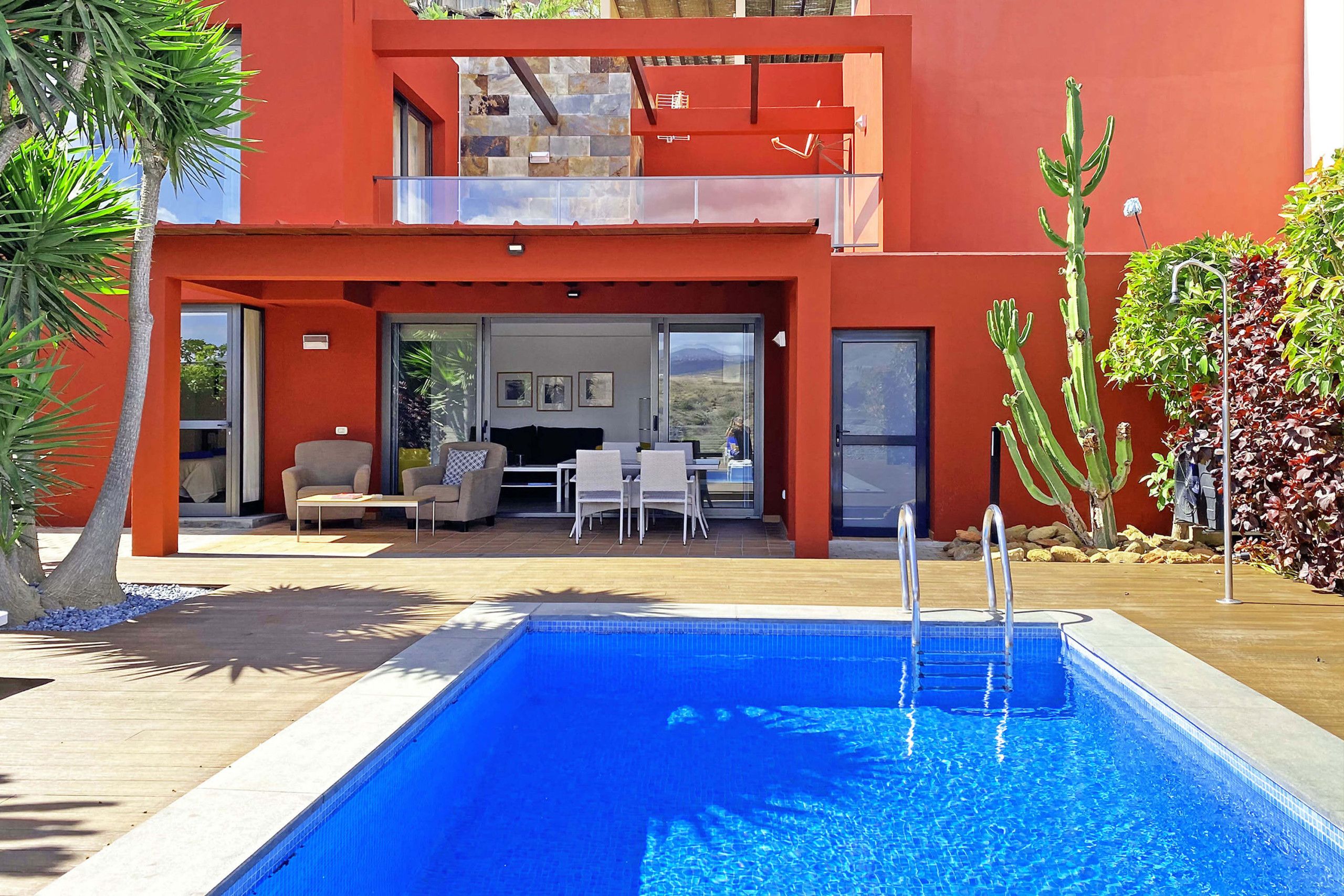 Een modern huis met een zwembad, tuinmeubilair en een cactusoort.