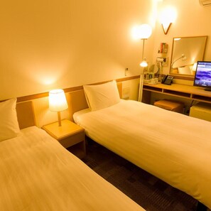 Habitación de hotel con dos camas individuales, lámparas de noche, un escritorio con computadora, un espejo y un teléfono.