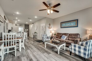 A spacious living room with a ceiling fan, a dining area with a white table and chairs, a kitchen area with cabinets and a refrigerator, and a cozy seating area with a brown leather couch and blue plaid chairs. - Spacious Condo with Spectacular Views (Branson)
