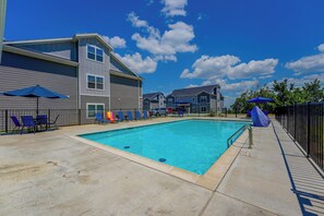 A swimming pool with lounge chairs and umbrellas, surrounded by a building with a grey facade. - Spacious Condo with Spectacular Views (Branson)