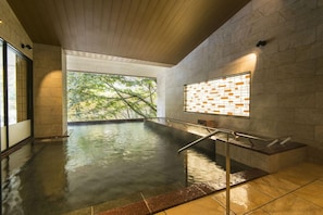 Un espace de bien-être avec un jacuzzi, des murs en pierre et une vue sur les arbres.