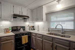 A modern kitchen with white cabinetry, a stainless steel sink, and a window with blinds. - Walk to Beach! Wareham Getaway w/ Patio (Wareham)