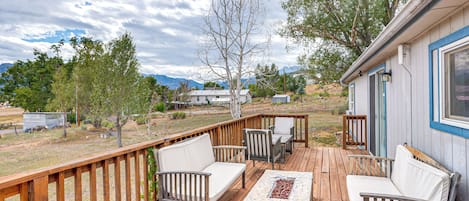 A wooden deck with outdoor furniture, a fire pit, and a view of mountains and trees in the background.