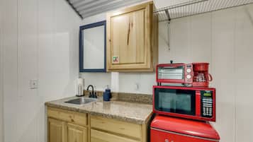 A compact kitchen with wooden cabinets, a granite countertop, a sink, a red Hamilton Beach microwave, and a coffee maker.