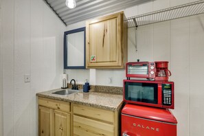 A compact kitchen with wooden cabinets, a granite countertop, a sink, a red Hamilton Beach microwave, and a coffee maker.