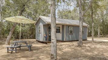 A small cabin with a porch, a picnic table, and a covered area with a patterned umbrella.