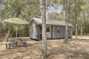 A small cabin with a porch, a picnic table, and a covered area with a patterned umbrella.