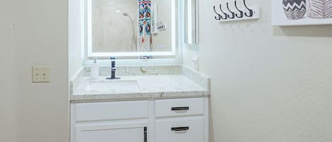 Un baño con lavamanos blanco, un espejo, toallero y una planta en maceta.