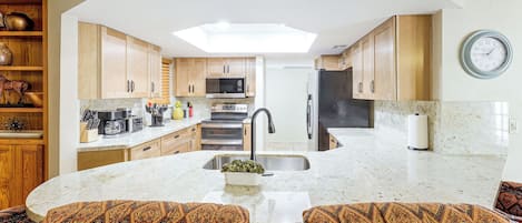 A kitchen with a central island, wooden cabinets, a microwave, oven, and a clock on the wall.