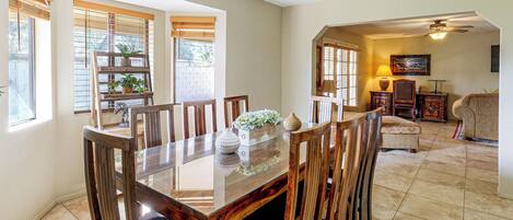 A dining area with a wooden table and chairs, a ceiling fan, and a view of the outdoors through large windows.