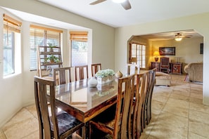 A dining area with a wooden table and chairs, a ceiling fan, and a view of the outdoors through large windows. - Home w/ Fenced Yard! 2 Mi to Dtwn Casa Grande (Casa Grande)