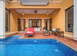 Zona de piscina amb una cadira de relaxació vermella, una taula de fusta i un ventilador de sostre.
