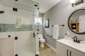 Un bagno moderno con box doccia in vetro, un water, un lavandino con specchio e un portasciugamani.