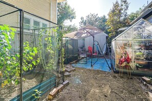 A fenced garden area with a greenhouse, a covered seating area, and a variety of plants. - Historic Des Moines Home: Great for Families! (Des Moines)