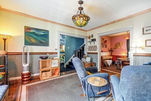 Ein Wohnzimmer mit blauem Sessel, Holzschrank, farbigem Gemälde und einer Treppe zu einem anderen Raum.